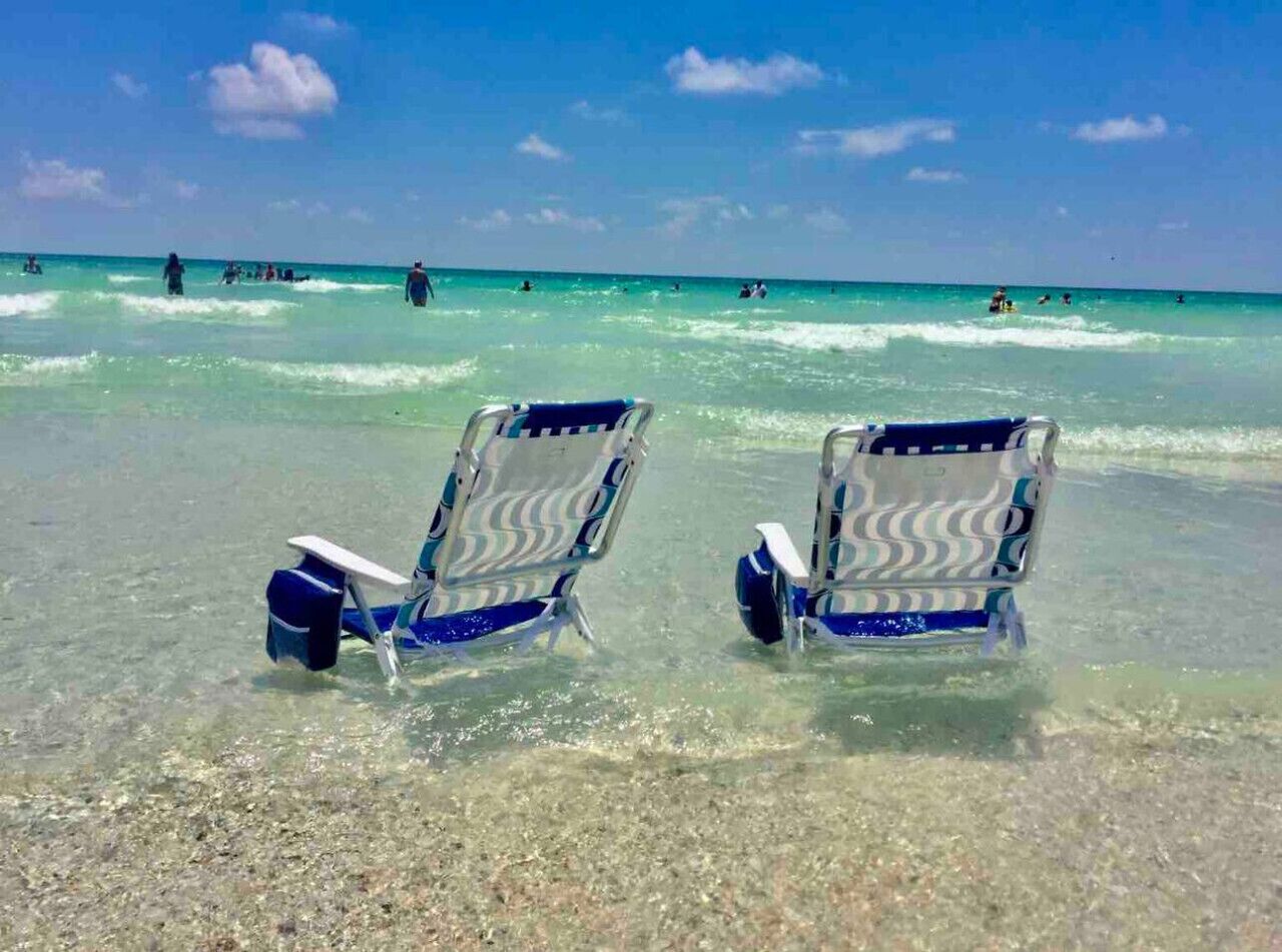 Two beach chairs on the shore with clear turquoise water and a few people in the distance.