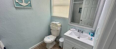 A bathroom with a toilet, sink, and mirror. There is a towel rack above the toilet and a rug on the floor.