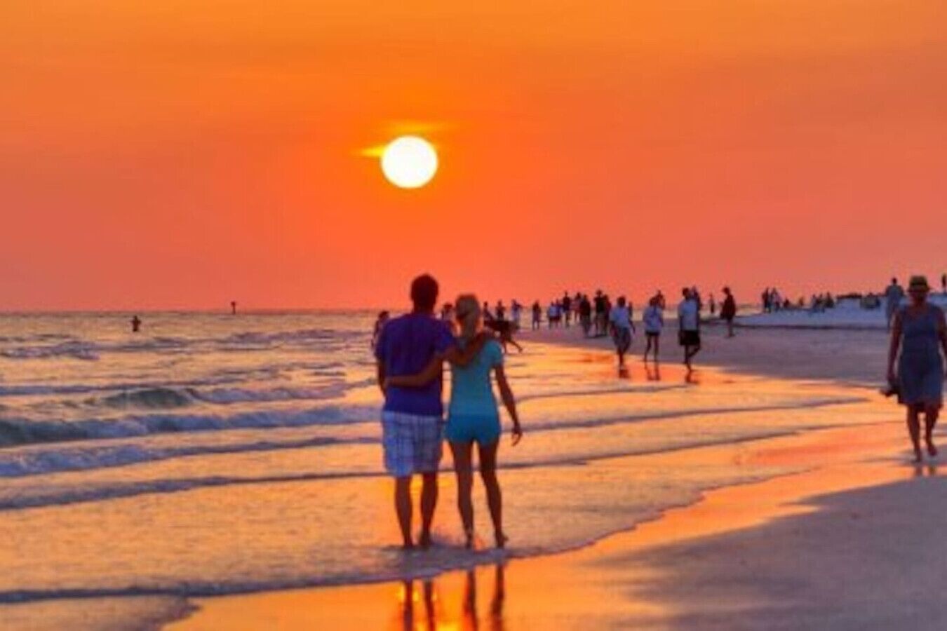 Cena de praia com pessoas caminhando pela costa ao pôr do sol.
