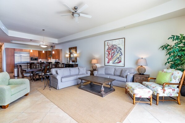 A modern living room with a grey sofa set, a coffee table, and a dining area with wooden cabinets and a kitchen in the background. - Turquoise Place 2807C by Liquid Life (Orange Beach)