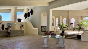 Eine großzügige Lobby mit hoher Decke, einem Empfangsbereich, einem Glastisch mit Dekoration und einer Treppe zu den oberen Stockwerken.