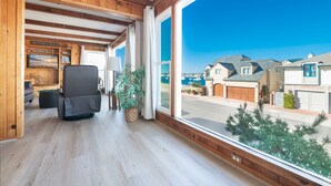 Una habitación con un ventanal grande, vigas de madera, un televisor, un sofá y vistas a casas y agua.