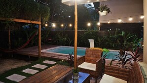 Un espace extérieur aménagé en terrasse, avec une piscine, des meubles en osier et des guirlandes lumineuses.