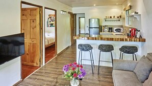 Un espace de vie compact comprenant un coin cuisine, un espace repas avec des tabourets de bar, un canapé et un téléviseur.