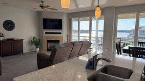A modern living room with a fireplace, a sofa, a television, and a view of a body of water through large windows.