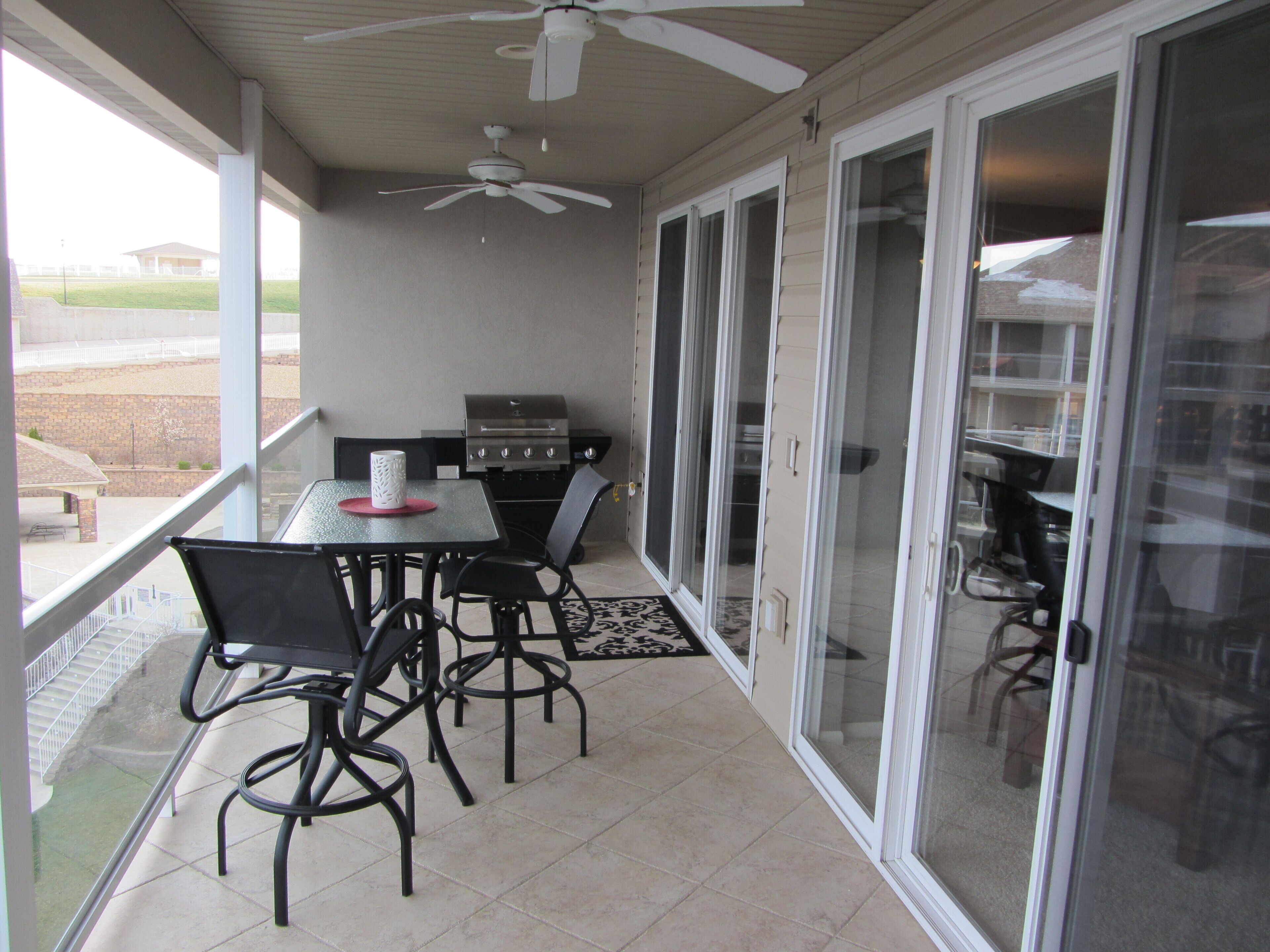 Une terrasse couverte avec une table et des chaises, un barbecue et un ventilateur de plafond.