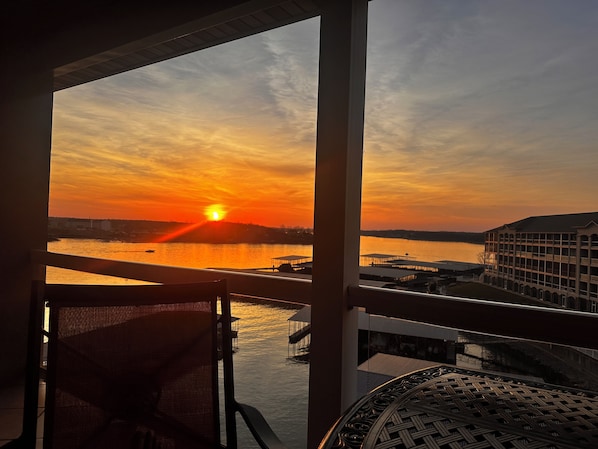A sunset view from a balcony overlooking a body of water, with a building and dock in the background.