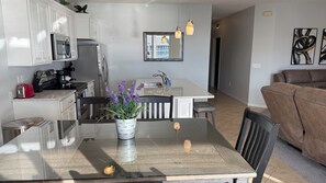 A modern kitchen with white cabinets, a stainless steel refrigerator, and a dining area with a table and chairs.