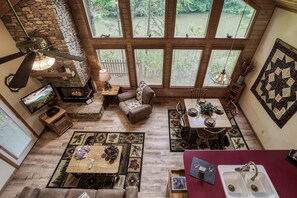 A cozy interior with a stone fireplace, wooden furniture, and large windows overlooking a natural landscape.
