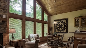 Una sala de estar acogedora con chimenea, ventanas amplias, comedor y cocina con armarios de madera.