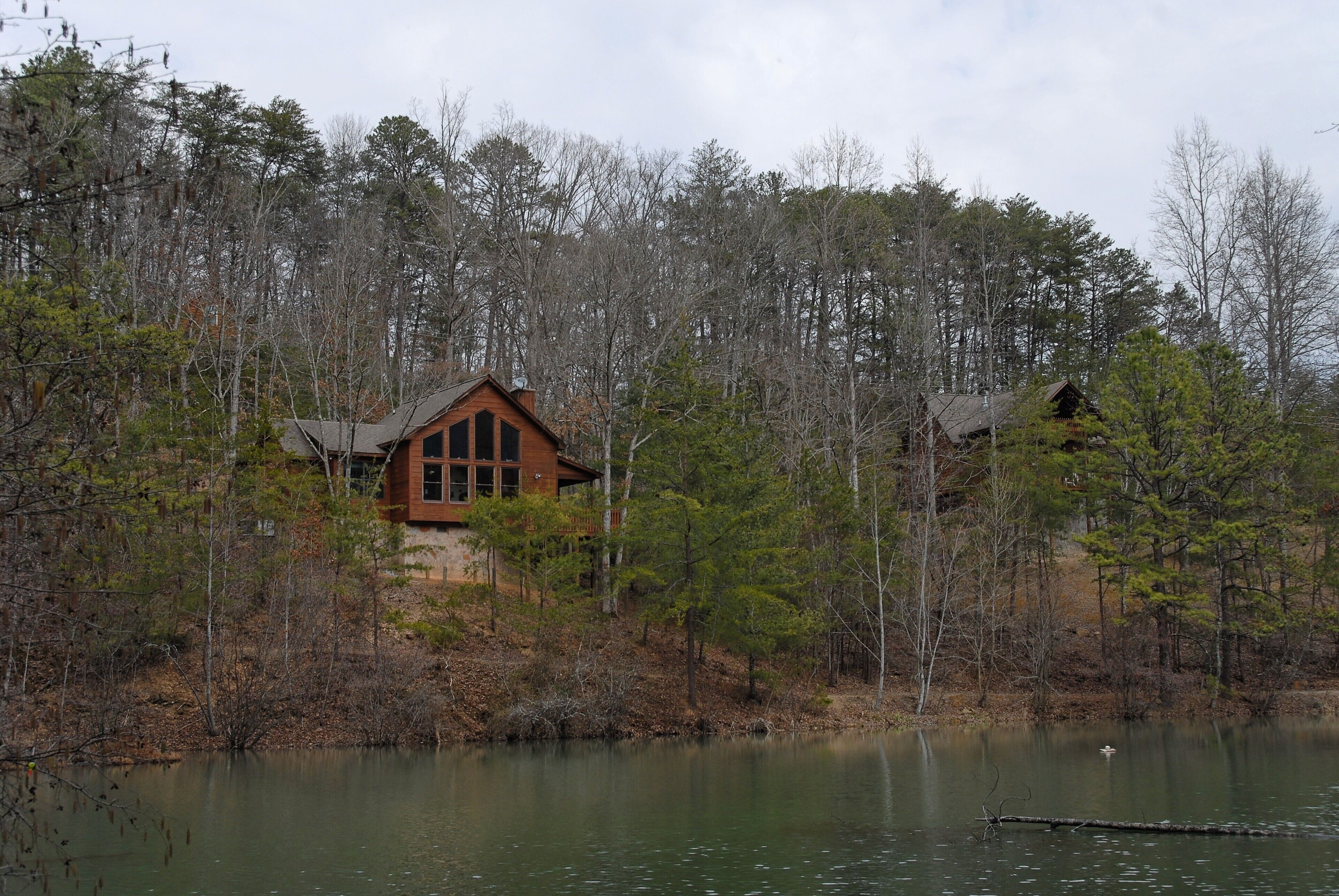 Une cabane entourée d’une forêt, avec un lac en premier plan.