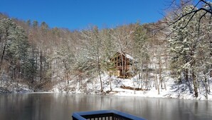 Una cabaña junto a un lago, con un muelle de madera y árboles cubiertos de nieve.