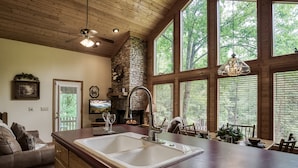 Una cocina con chimenea de piedra, techo de madera y ventanas amplias.
