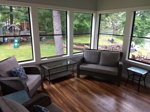 A cozy room with large windows, a wooden floor, a grey sofa, and a small table. - Getaway on BEAUTIFUL Balsam Lake, WI (Balsam Lake)