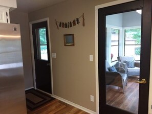 A hallway with a refrigerator, a door leading to a living area with a sofa and a window, and a wall-mounted picture frame. - Getaway on BEAUTIFUL Balsam Lake, WI (Balsam Lake)