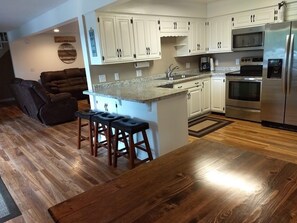 A modern kitchen with white cabinets, a stainless steel refrigerator, and a wooden dining table. - Getaway on BEAUTIFUL Balsam Lake, WI (Balsam Lake)