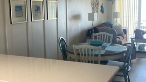 A kitchen with a white countertop, cabinets, and a dining area with a table and chairs. - It’s Beachy Keen!         (New Smyrna Beach)