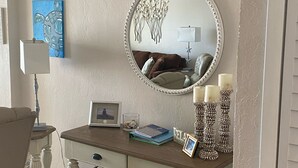 A room with a vanity table, a round mirror, a blue artwork, a lamp, and decorative candles. - It’s Beachy Keen!         (New Smyrna Beach)
