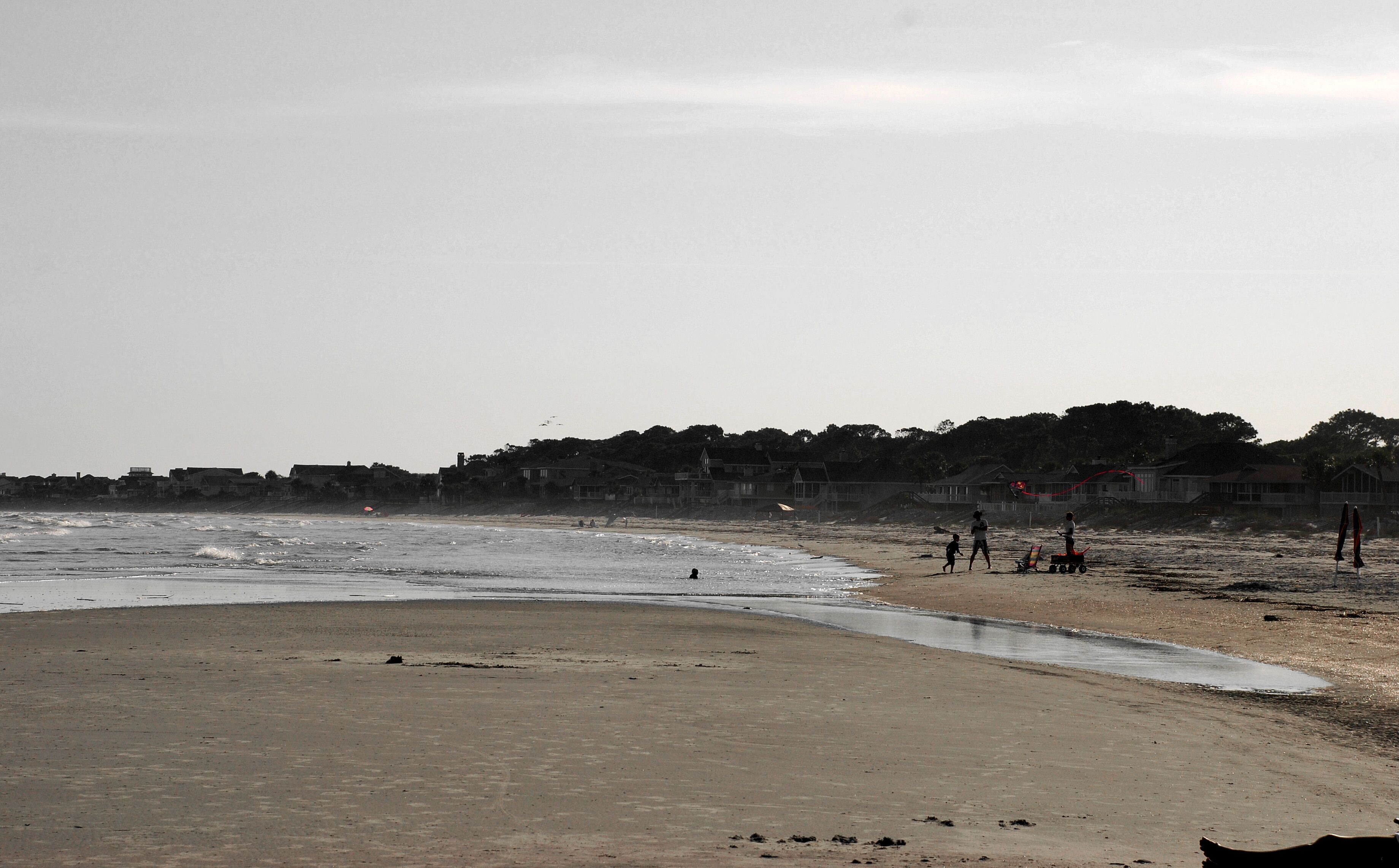Een strand met een zandstrand, enkele mensen en huizen op de achtergrond.