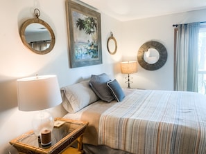 A neatly arranged hotel room with a large bed, a bedside table with a lamp, a small table with a lamp, and a painting on the wall.