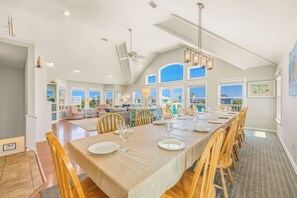 A spacious dining area with a long table set for a meal, large windows offering a view, and a ceiling fan.