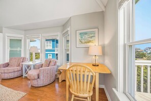 Settle into your coastal retreat with abundant natural light, warm wood floors, and cozy seating. Large windows frame bright blue skies and the charming neighborhood just outside your door.
