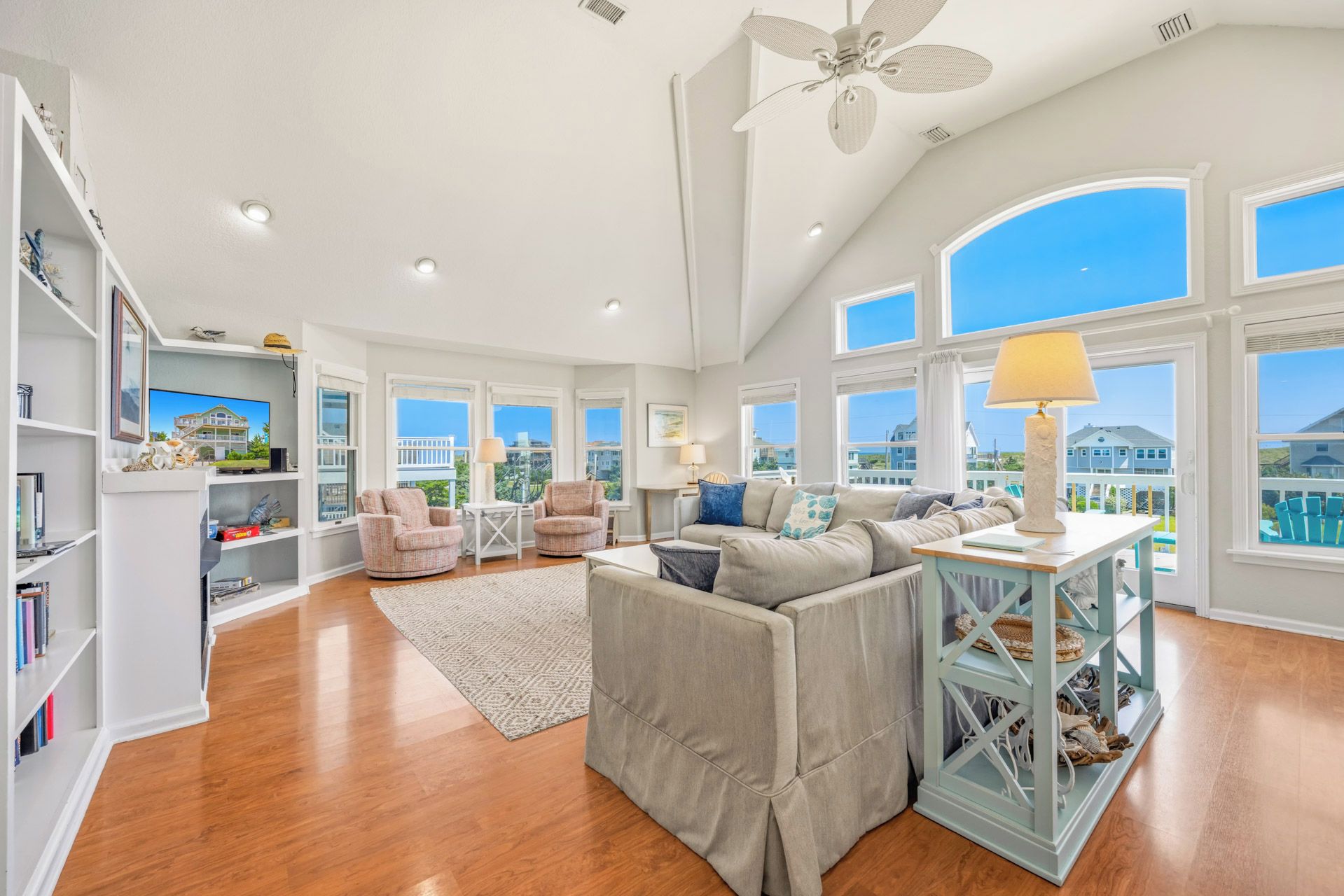 A spacious living room with a high ceiling, large windows, and a view of the outside.