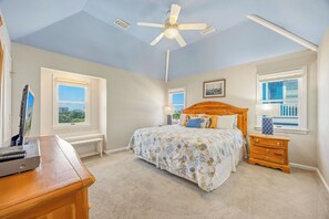 Une chambre à coucher avec un lit, un ventilateur de plafond, une table de chevet, une lampe et une fenêtre donnant sur un beau paysage.