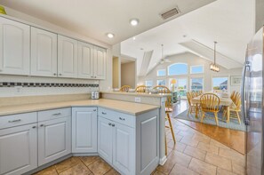 A kitchen with white cabinets, a central island, and a dining area with wooden chairs.