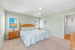 A bedroom with a single bed, a nightstand, a dresser, a ceiling fan, and a window with shutters.
