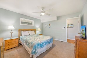 A bedroom with a bed, nightstands, a ceiling fan, and a door leading to another room.