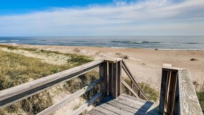 Ein Holzsteg führt zu einem Strand unter blauem Himmel.
