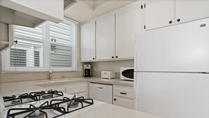 Une cuisine avec des meubles blancs, une cuisinière à gaz, un four à micro-ondes et une machine à café.