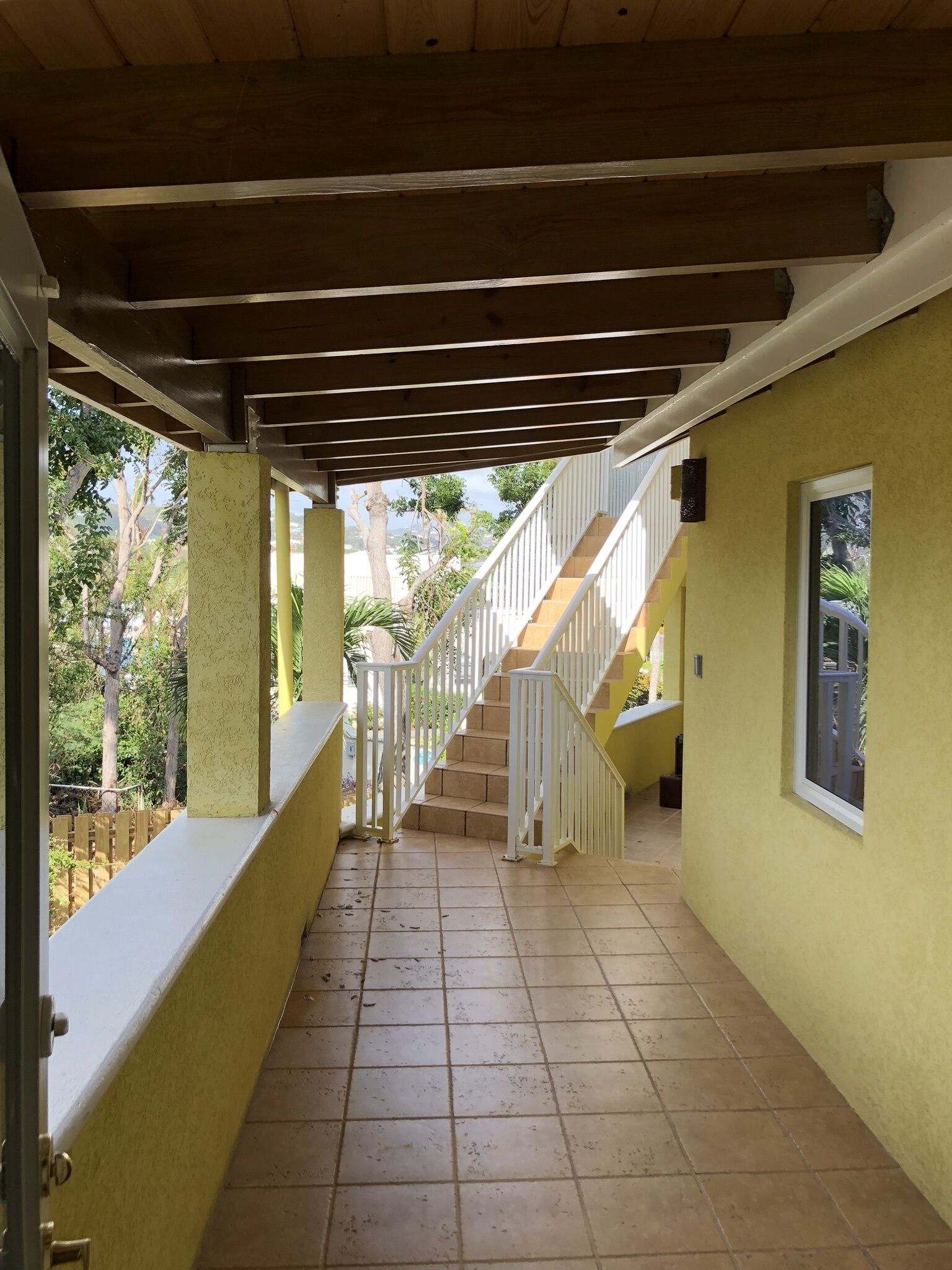 Ein überdachter Gang mit Fliesenboden, weißen Geländern und einer Treppe, die zu einer oberen Ebene führt.