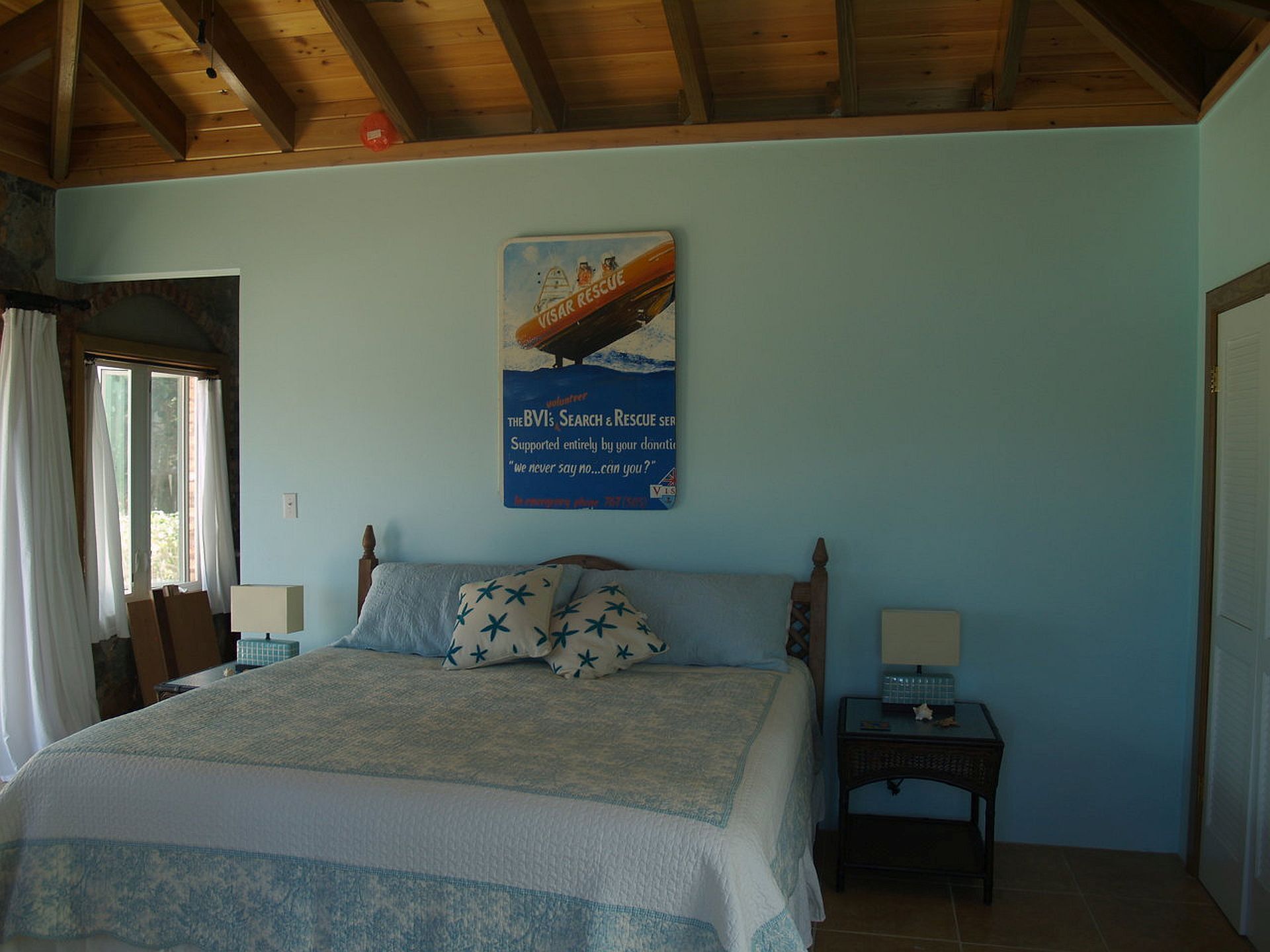 A bedroom with a bed, two bedside tables, a window with curtains, and a poster on the wall.