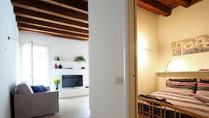 A living room with a sofa, TV, and a bed with a wooden headboard. - Appartamento al Duomo in the Historical center of the city (Vicenza)