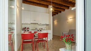 A compact kitchen with white cabinets, a dining table with red chairs, and a vase of red tulips on a counter. - Appartamento al Duomo in the Historical center of the city (Vicenza)