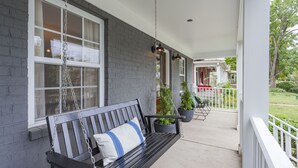 Une véranda avec un banc noir, des balustrades blanches et des plantes suspendues.