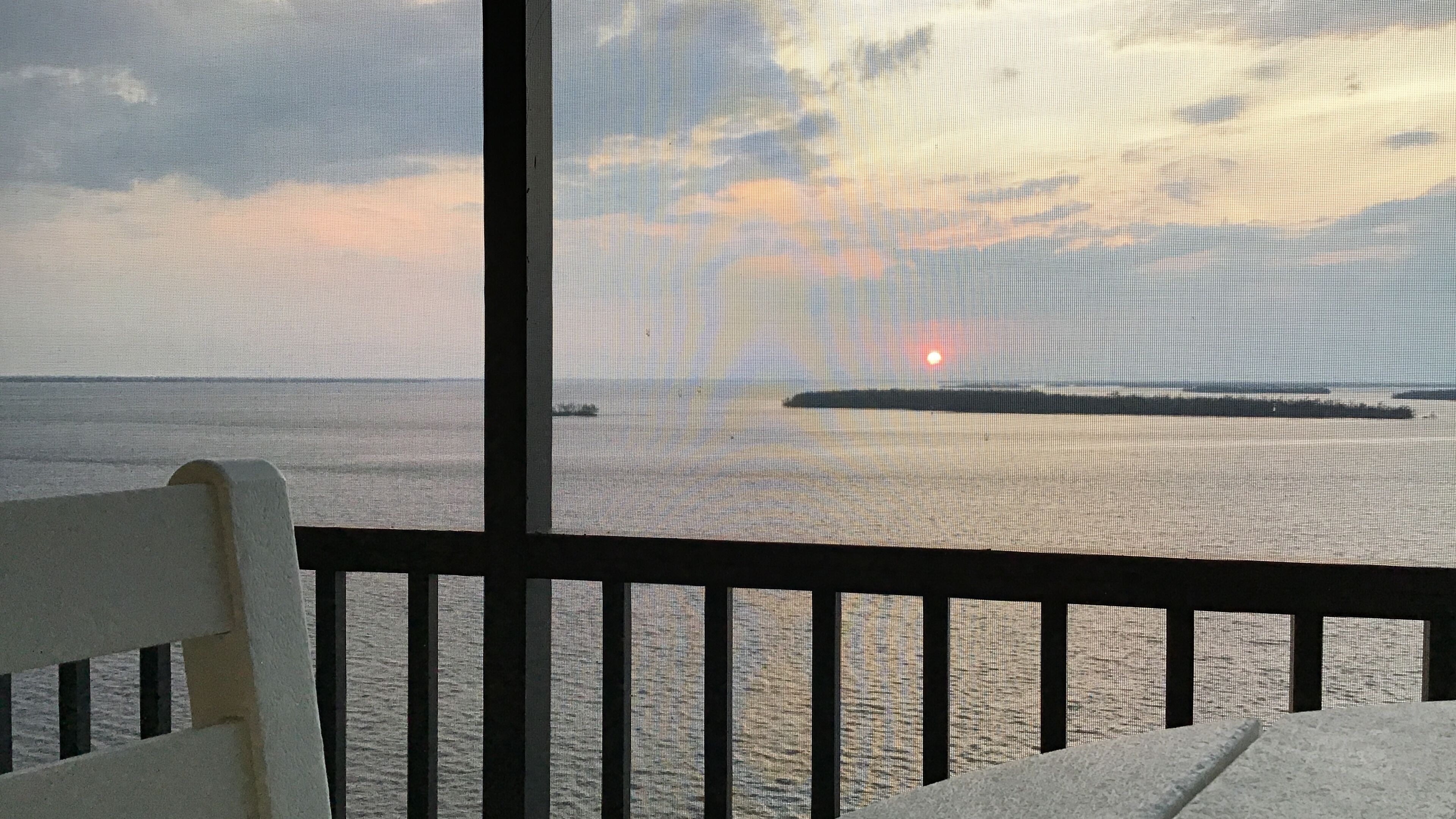 A view from a balcony with a railing, overlooking a calm sea and a distant island.