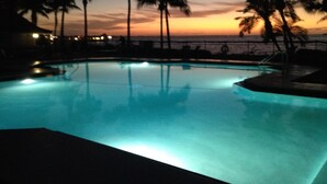 Una piscina con vista al atardecer, palmeras y una barandilla.