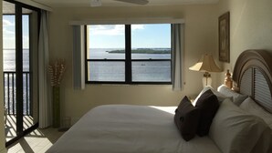 Un dormitorio con un ventanal que ofrece vistas al agua, un ventilador de techo y una cama con almohadas.