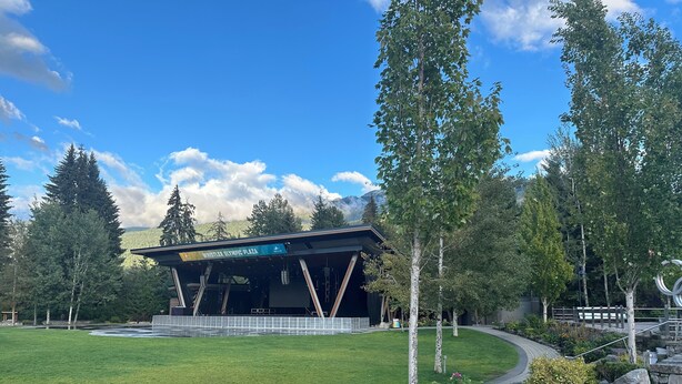 A Whistler Olympic Plaza with a large open-air stage, surrounded by a well-maintained lawn and trees.