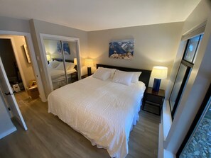 Ein Hotelzimmer mit einem großen Bett, einem Spiegel, einem Bild an der Wand und einem Nachttisch mit einer Lampe.