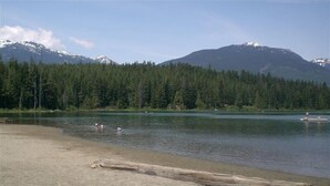 A lakeside view with a sandy beach, a wooden log, and a rowboat.