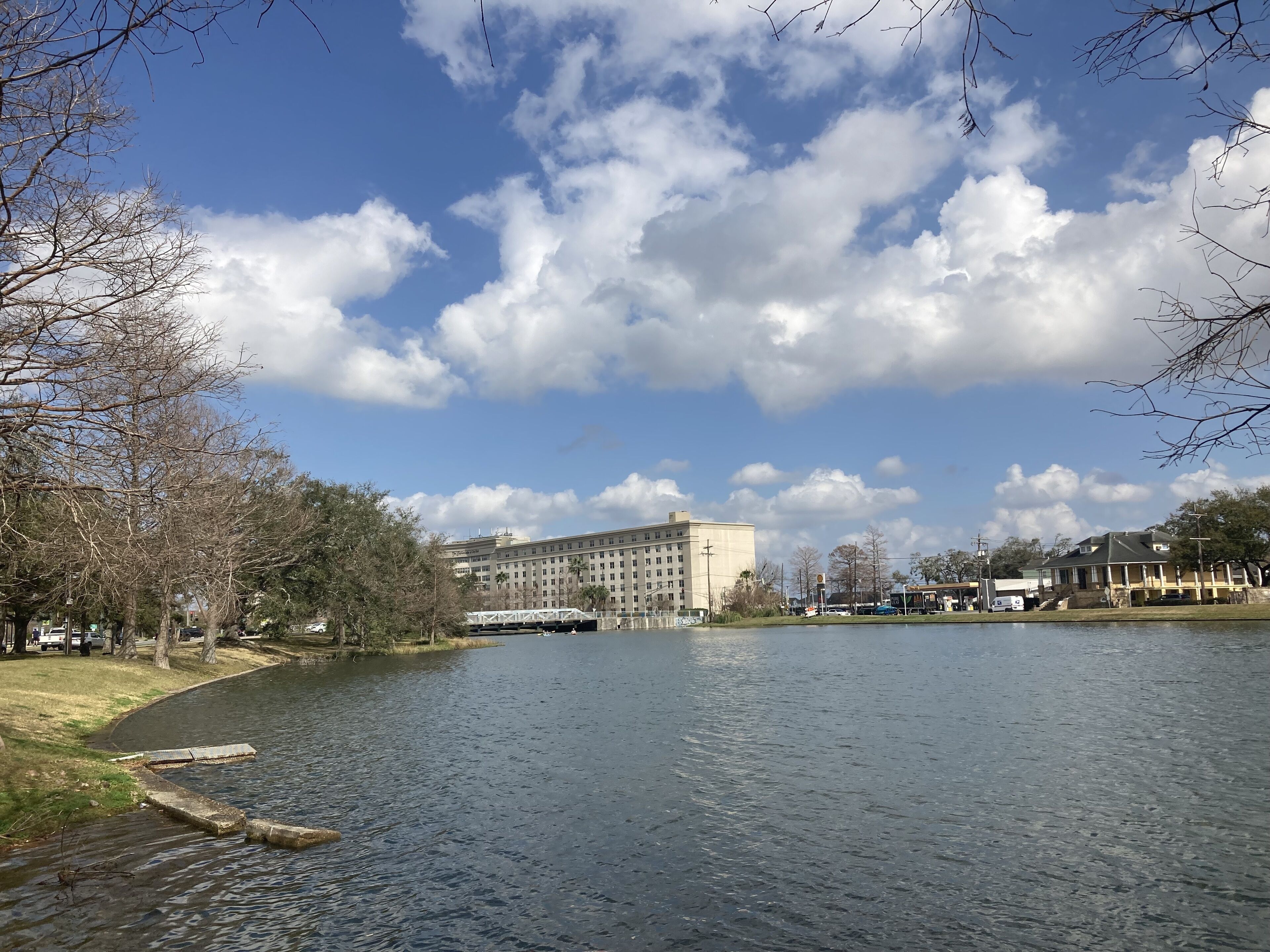 A large building with multiple floors and a flat roof, situated by a calm body of water with a dock.