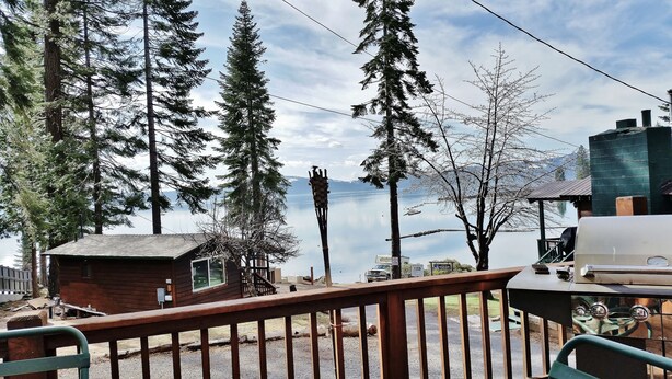 A cabin with a deck overlooking a lake, surrounded by tall trees.