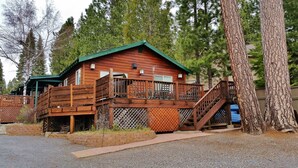 A wooden cabin with a deck and stairs, surrounded by trees.