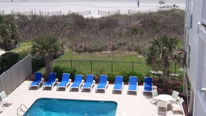 Zona de piscina con sillas reclinables azules, una piscina pequeña y vista a la playa y el océano.