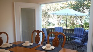 Un coin repas avec une table en bois dressée pour le repas, des chaises et une terrasse extérieure avec des chaises à rayures bleues et un grand parasol.