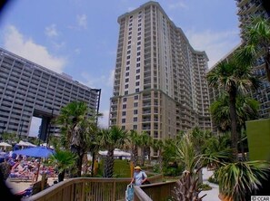 A high-rise hotel with multiple floors, a pool area with umbrellas, and palm trees. - 2 BR Royale Palms Oceanview #1103 POOL PASSES INCLUDED! (Myrtle Beach)